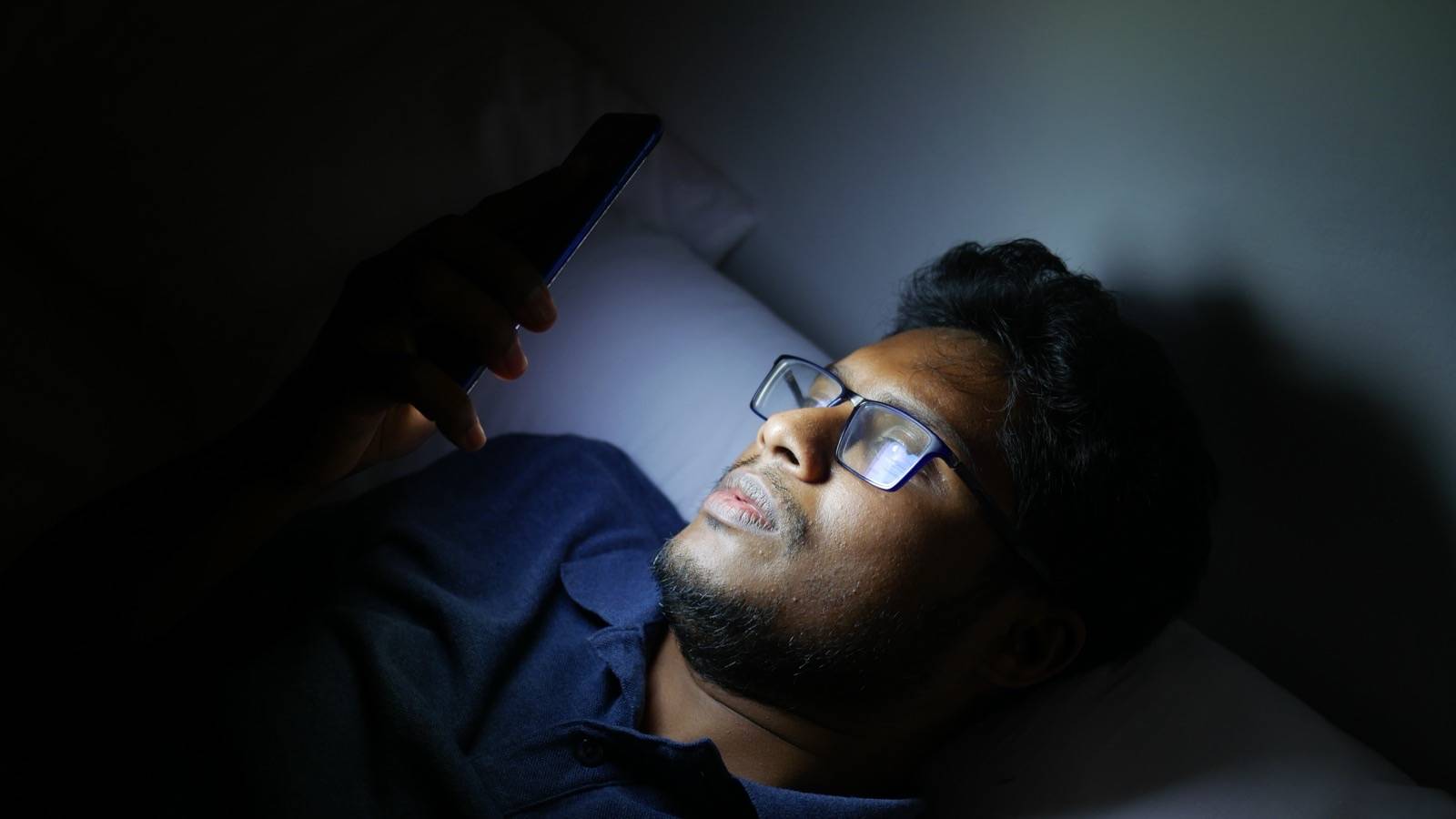 Young man lying in bed, looking at his phone late at night