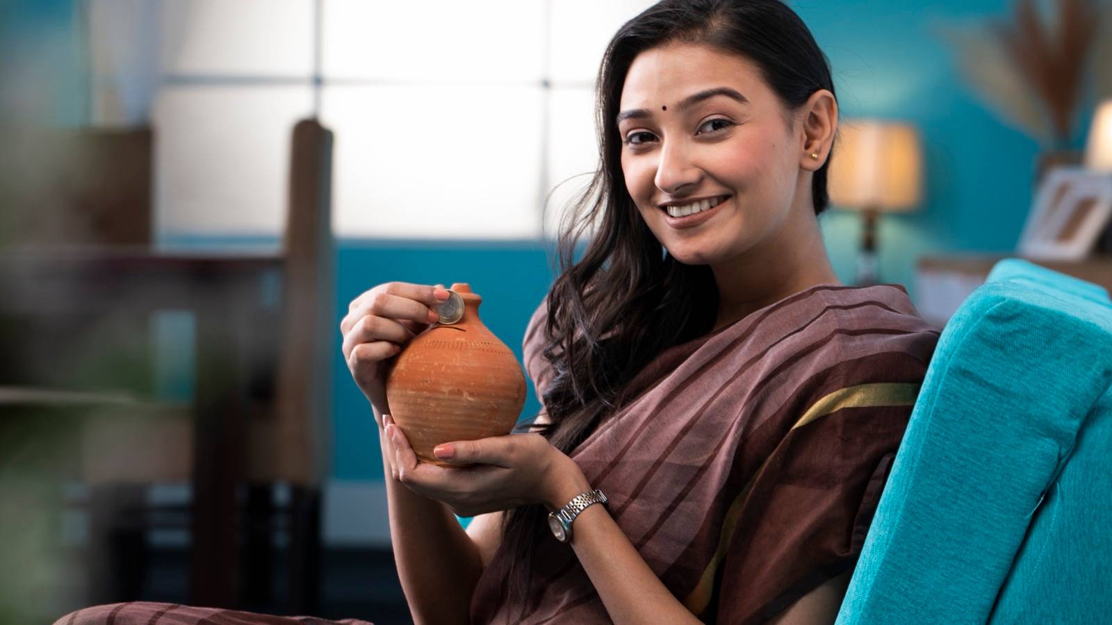 Woman dropping a coin into a clay money pot at home