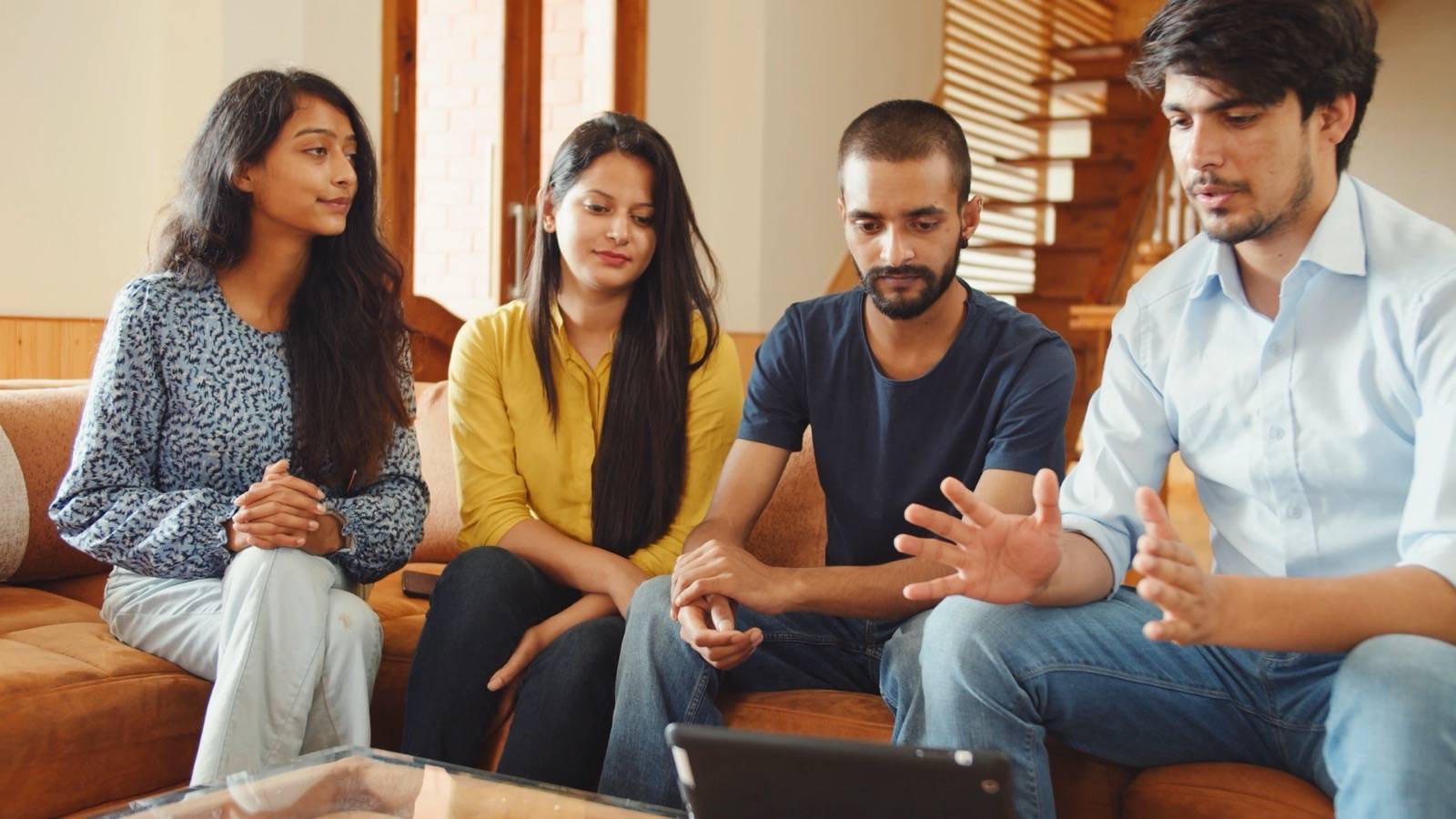 Four young adults talking together on a sofa at home