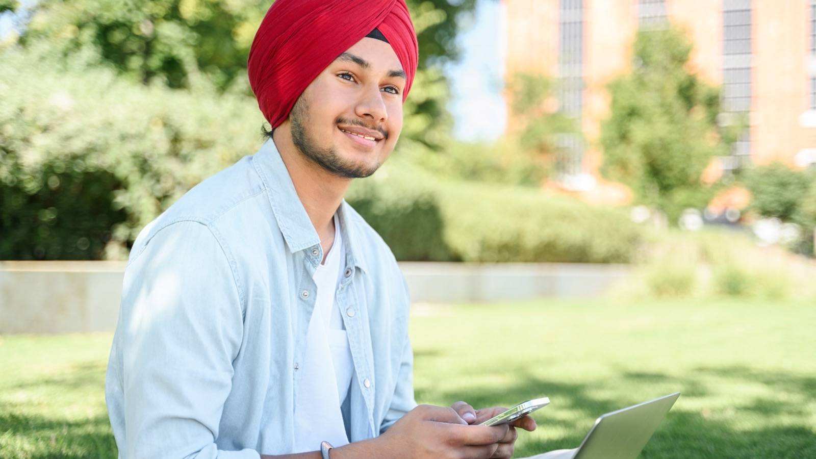 Student using a phone and laptop on a campus lawn